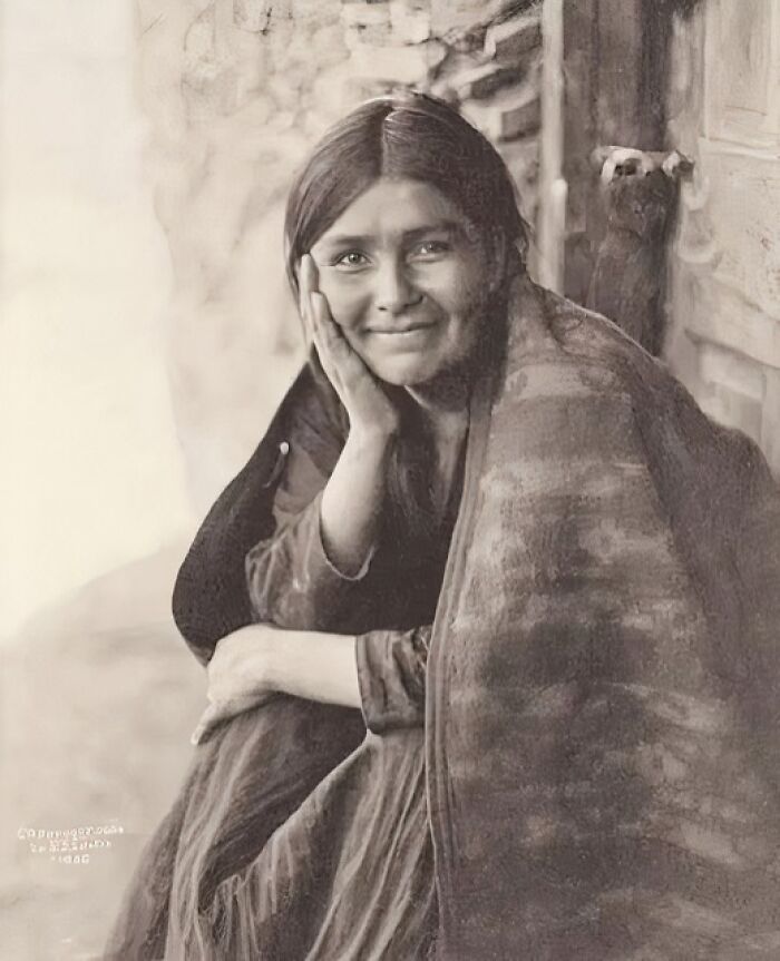 Young woman wrapped in a blanket sitting and smiling in an antique historical photograph from the past.