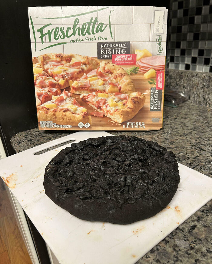 Burnt frozen pizza on a cutting board in a kitchen, showing a common cooking fail with blackened crust.