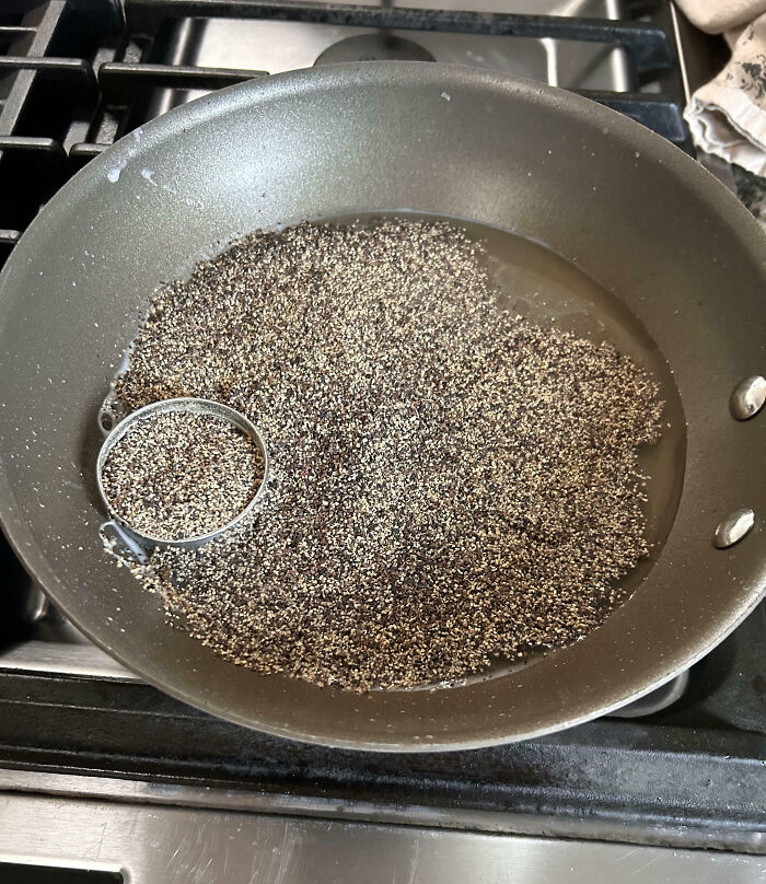 Pan filled with hundreds of black pepper granules spilled during a cooking fail on a stovetop burner.
