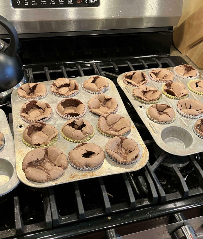 Burnt and c*****d chocolate cupcakes in muffin tins on a stove, showcasing cooking fails and kitchen accidents.