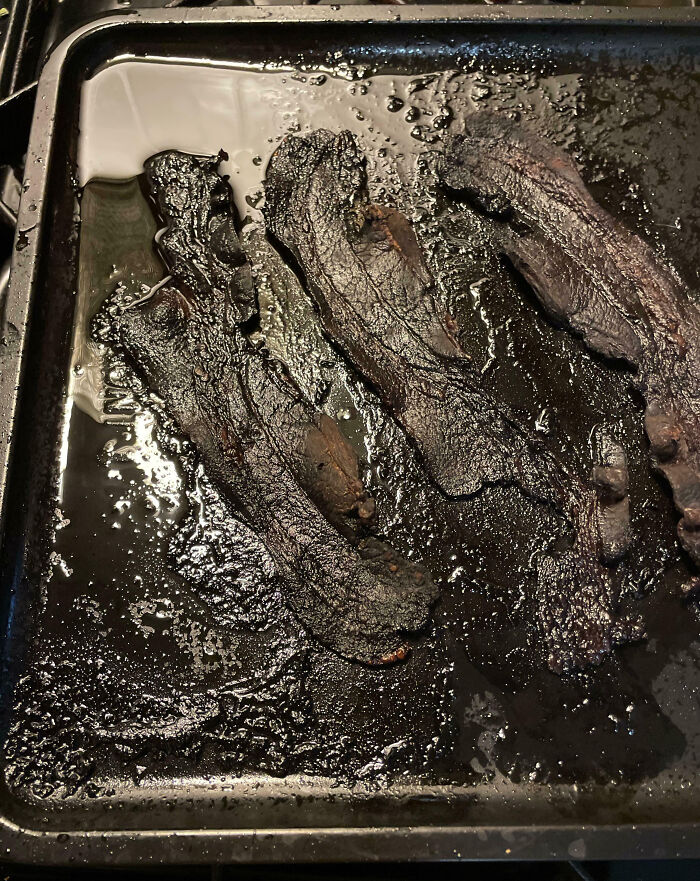 Burnt bacon slices on a greasy baking tray showcasing a cooking fail and accident in the kitchen.