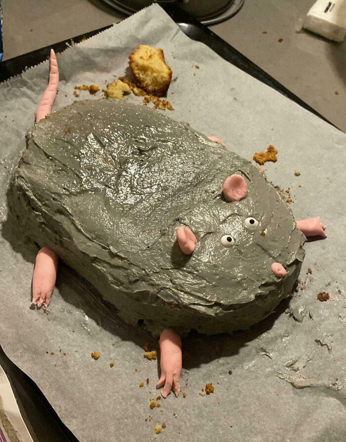 A poorly decorated gray cake resembling a rat with pink fondant limbs and ears, showcasing a cooking fail.