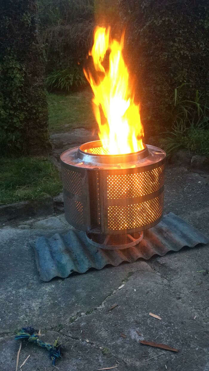 DIY project fire pit made from a repurposed metal drum with bright flames in an outdoor garden setting.