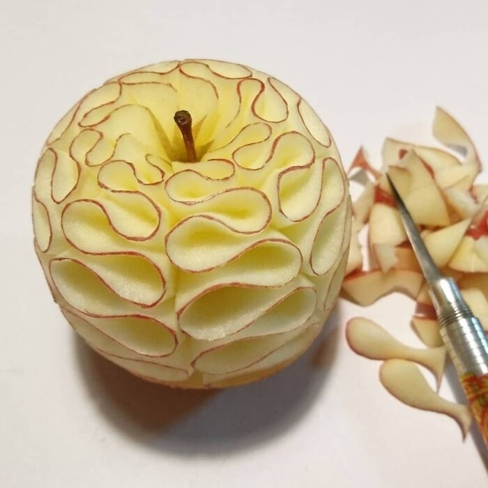 Intricate apple carving DIY project showing detailed patterns and carving tool on white background.