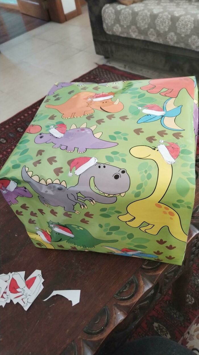 A DIY project wrapping a box with dinosaur paper and small Santa hats, showcasing creative and quirky DIY projects.