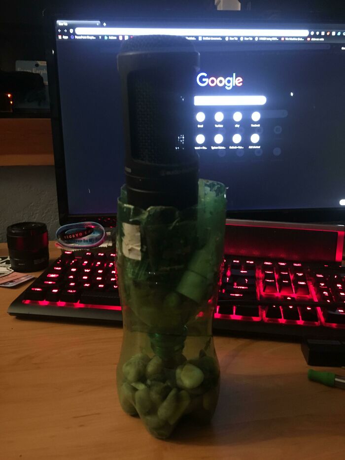 Homemade DIY project with a microphone placed inside a repurposed plastic bottle filled with stones on a desk.
