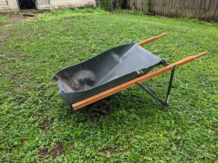 DIY wheelbarrow project with a plastic tub and wooden handles on green grass in a backyard setting