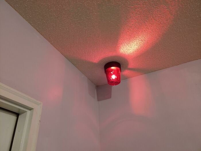 Red light DIY project installed in ceiling corner, casting glowing red reflections on textured ceiling and walls.