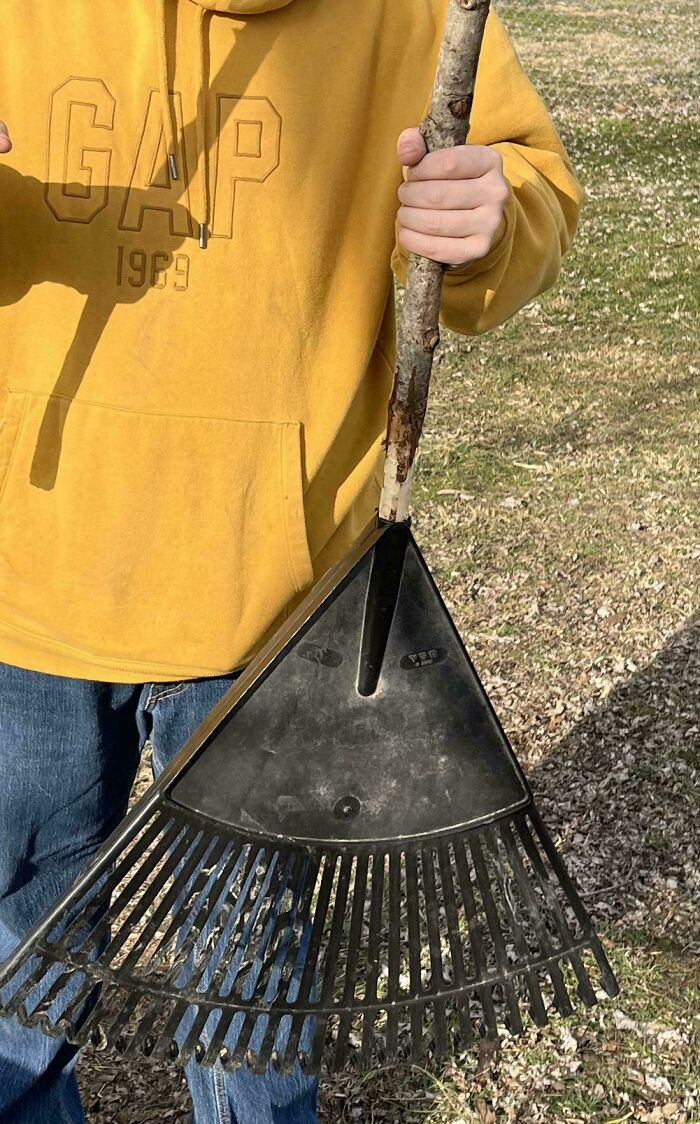 Person holding a DIY rake with a stick handle, showcasing a creative but unhinged DIY project outdoors.