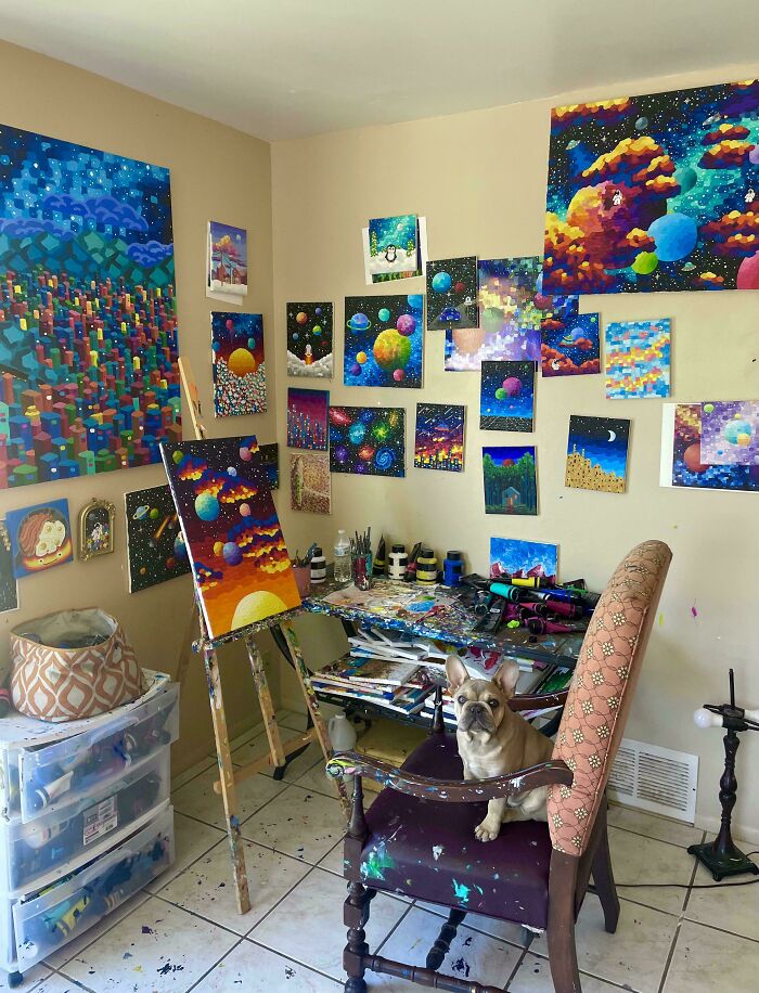 Art studio filled with colorful DIY projects, space-themed paintings on walls, and a dog sitting on a paint-splattered chair.