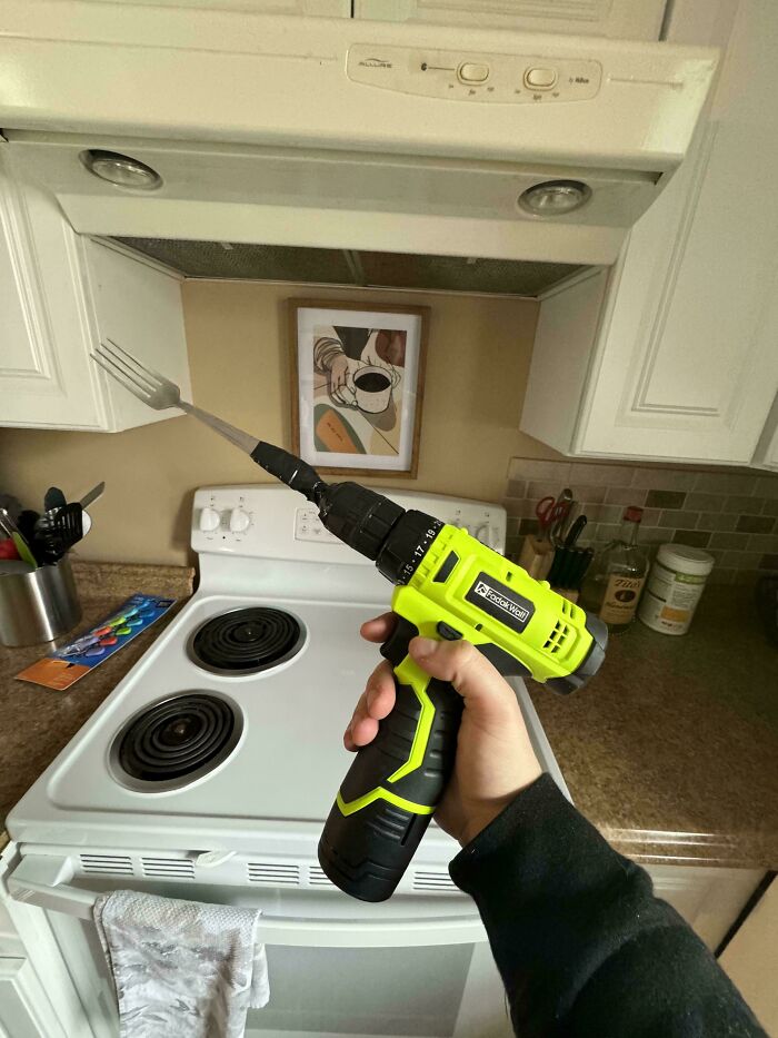 Person holding a drill with a fork attached in a kitchen, showcasing a creative and unusual DIY project idea.