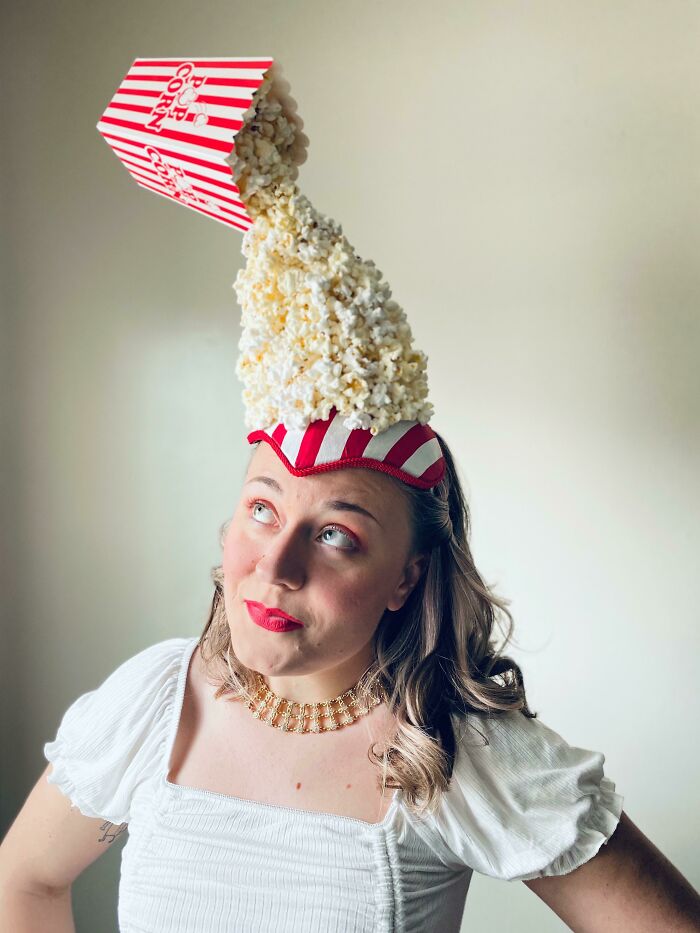 Woman wearing a creative DIY popcorn hat with popcorn spilling from a striped container, showcasing unique DIY projects.