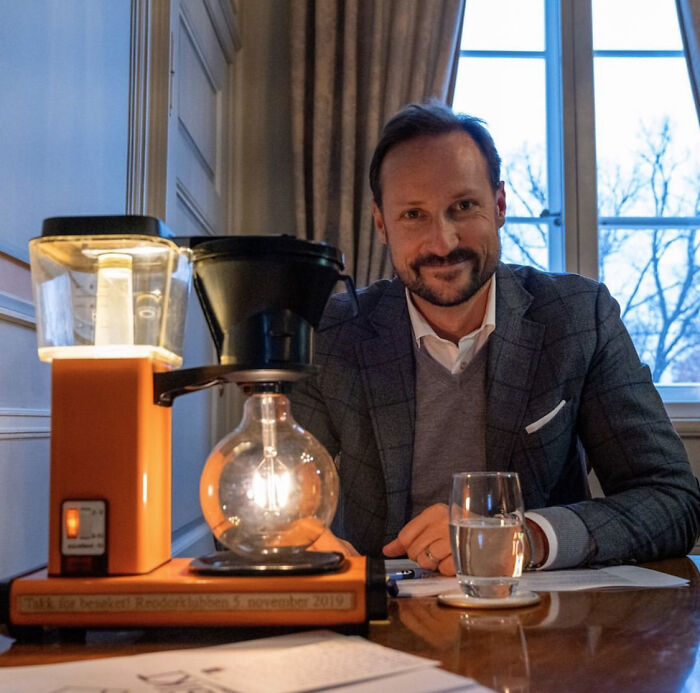 Man sitting at a table with a creative DIY project involving a light bulb and coffee maker parts indoors.