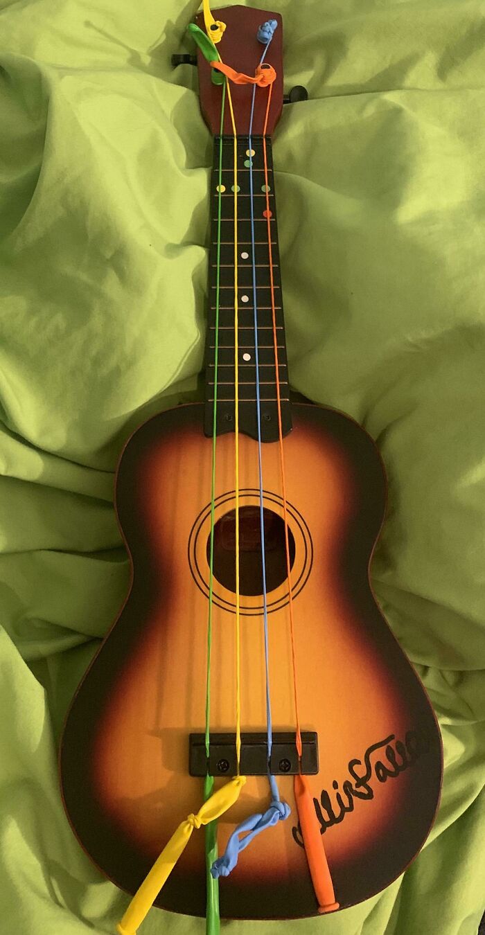 Ukulele with colorful balloon strings tied as DIY project on a green fabric background, showcasing creative DIY projects.