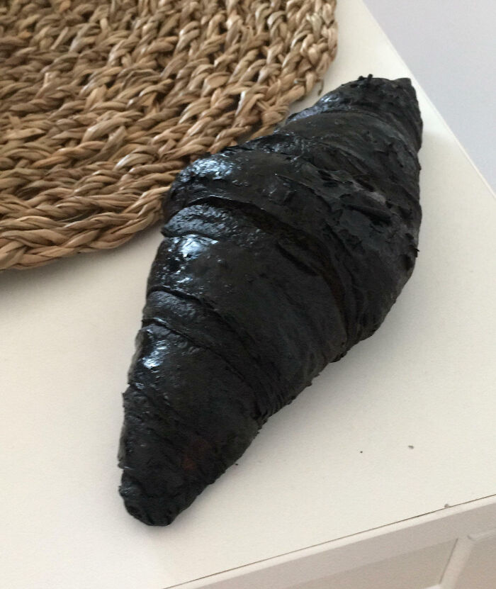 Burnt croissant on white table next to a woven placemat, showcasing a cooking fail and accident.