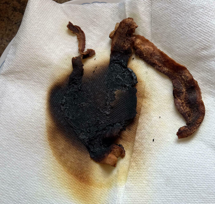 Burnt bacon pieces on a paper towel showing a cooking fail from a hilariously painful kitchen accident.