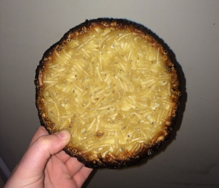 Hand holding a burnt mac and cheese dish showcasing a cooking fail with overcooked and charred edges.