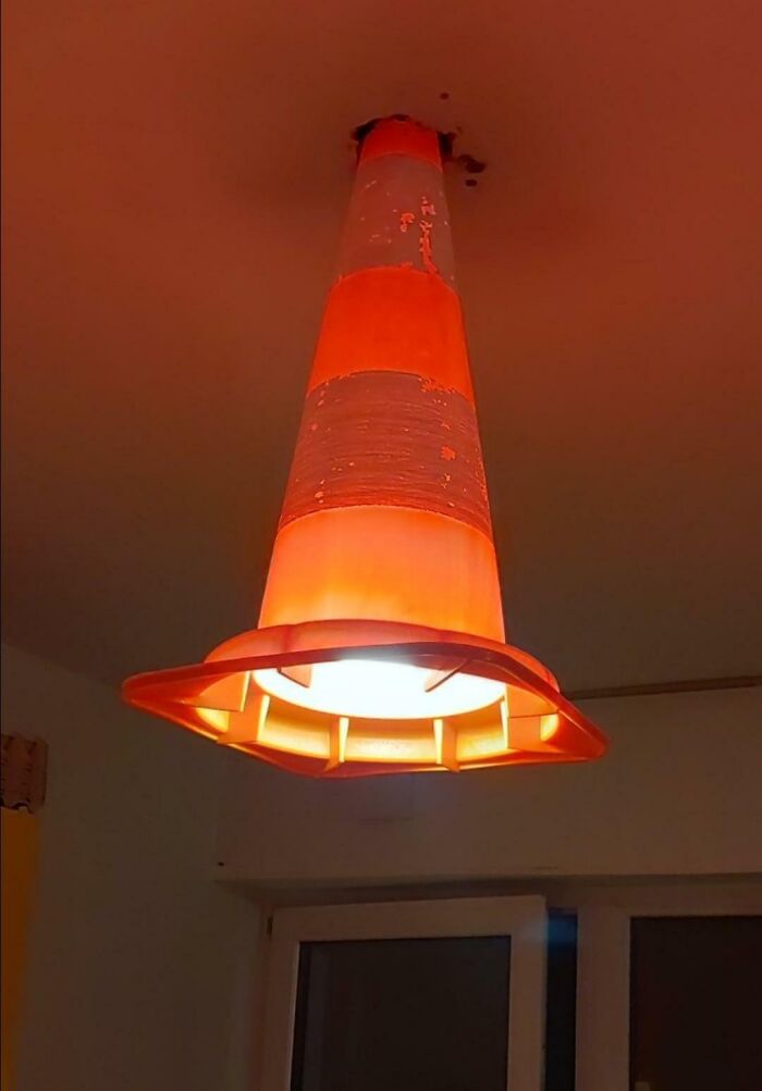 Orange traffic cone repurposed as a DIY light fixture hanging from a ceiling in a room.