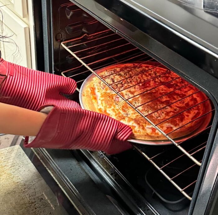 Hands with red oven mitts removing a pizza from an oven, one of the top Amazon finds on popular wishlists.