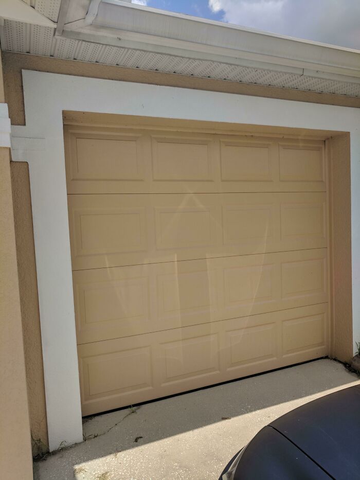 Beige garage door with faint white shapes that look like a spooky face requiring a double take.