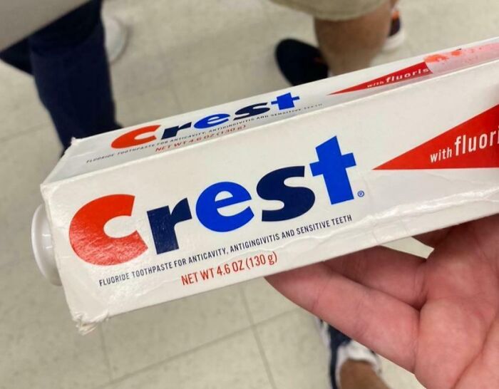 Hand holding vintage Crest toothpaste box, showcasing how things used to look with old packaging design.