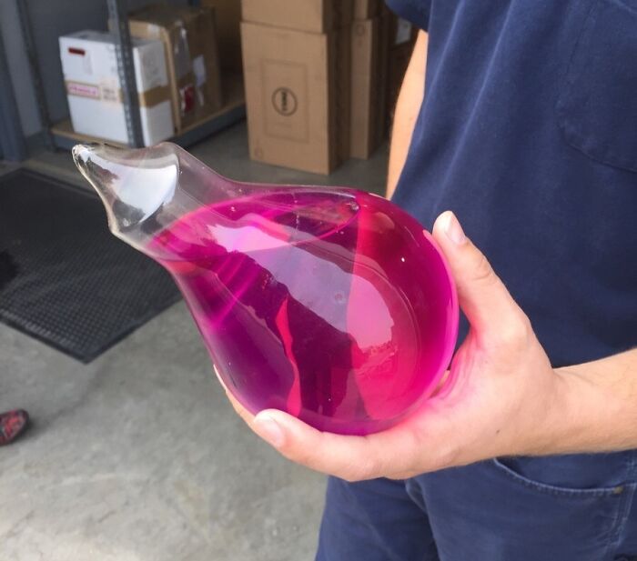 Hand holding a vintage glass water container filled with bright pink liquid, showing how things used to look.