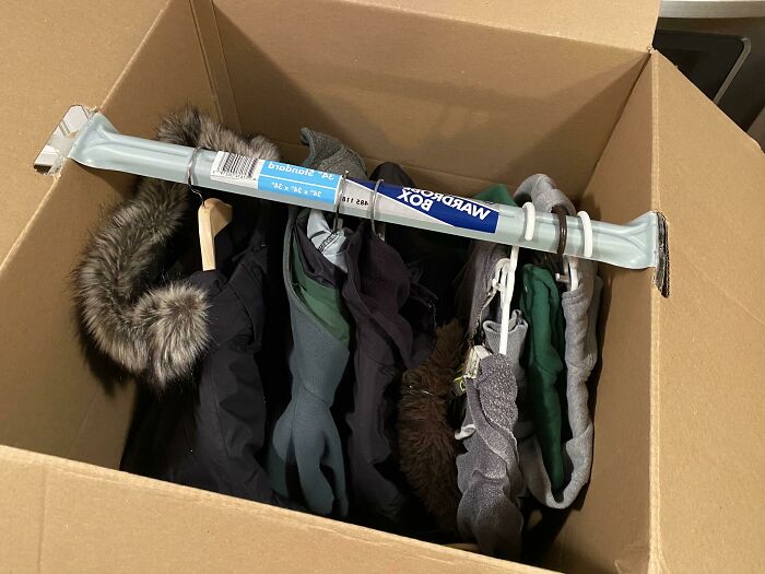 Cardboard box used as a closet with a wardrobe bar holding winter coats, showcasing clever solutions for overlooked storage issues.