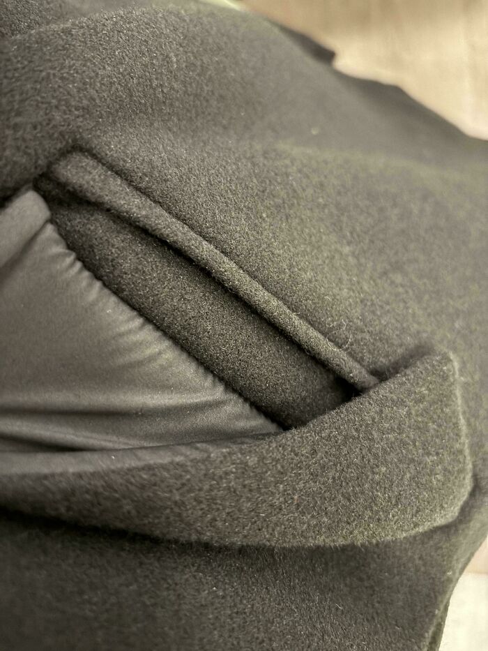 Close-up of a coat pocket showing a poorly aligned flap, illustrating a mildly infuriated mood ruined by small annoyances.