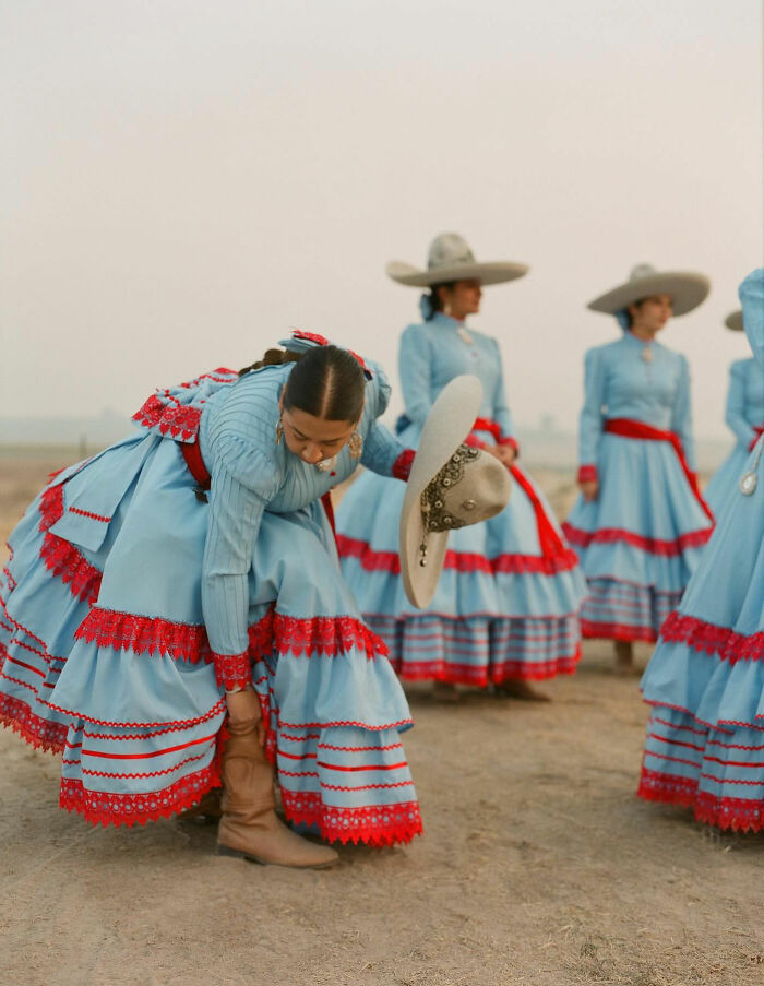 Female rodeo riders dressed in traditional blue and red attire preparing for performance outdoors on a dusty ground.