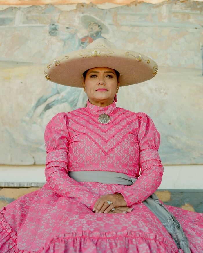 Female rodeo rider in traditional pink dress and wide-brimmed hat, showcasing strength and beauty in portrait style.