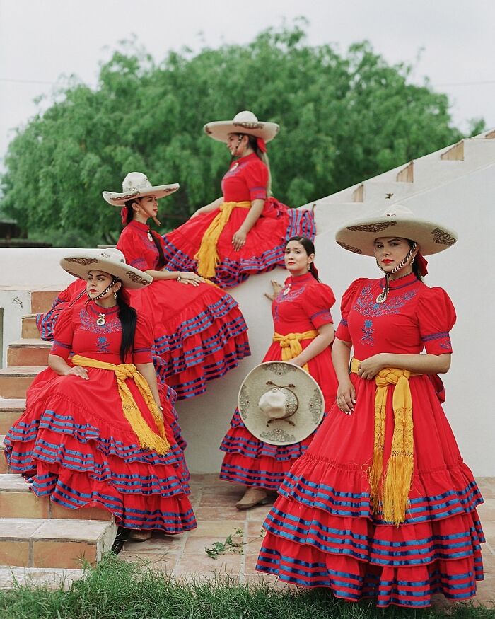 All-female rodeo riders dressed in vibrant traditional red dresses and wide-brimmed hats posing outdoors on steps.