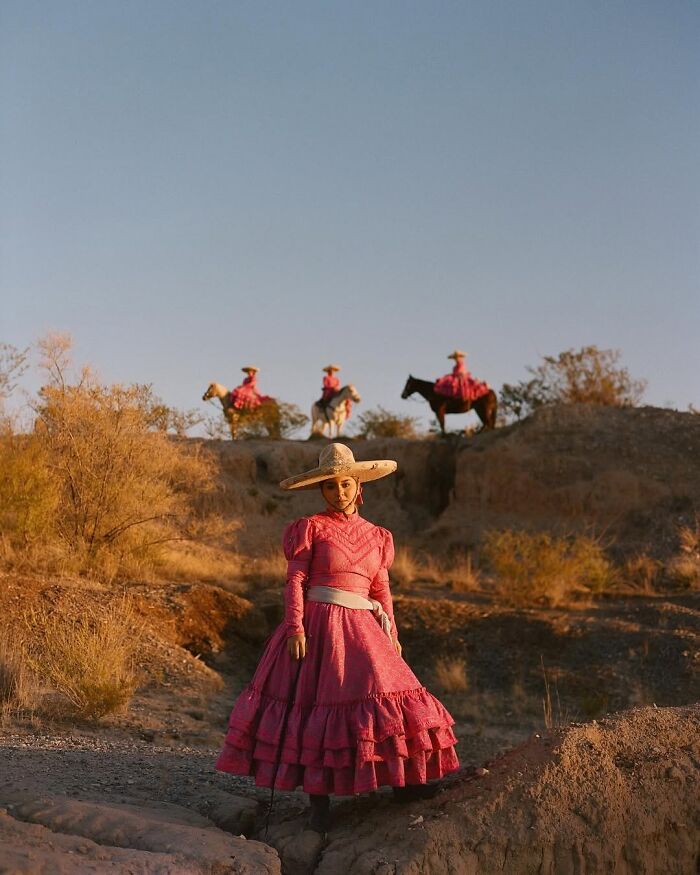 Female rodeo rider in traditional dress and hat, with three other all-female rodeo riders on horseback in background.