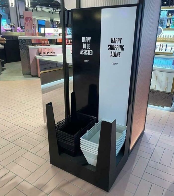 Black and white shopping baskets separated by signs saying happy to be assisted and happy shopping alone in a store.