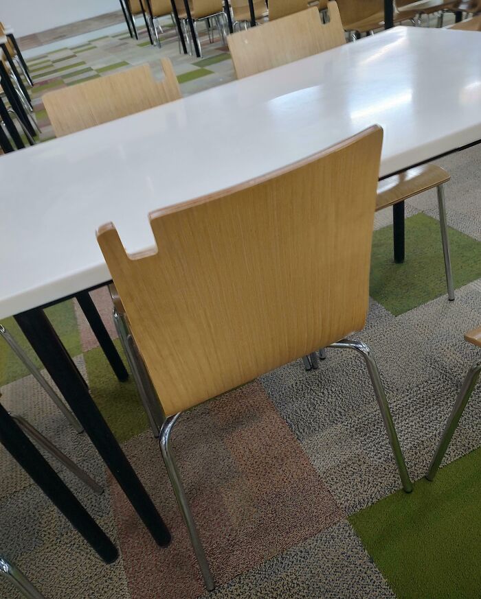 Wooden chair with a clever cutout design fitting neatly against a white table in a modern seating area.