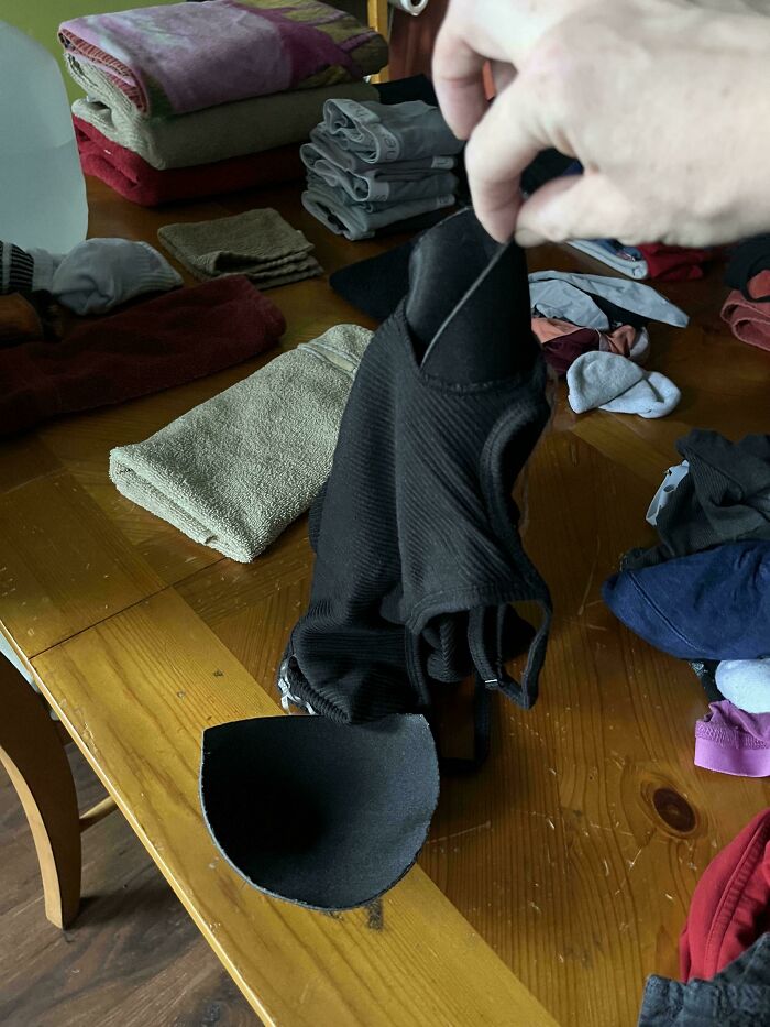 Hand holding broken bra strap with laundry on wooden table, illustrating what ruined mood for mildly infuriated people.