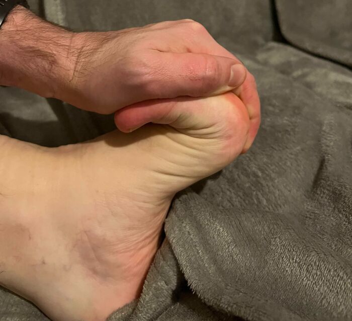 A hand gripping a foot against a grey textured fabric, showing an unusual bending of the human body part.