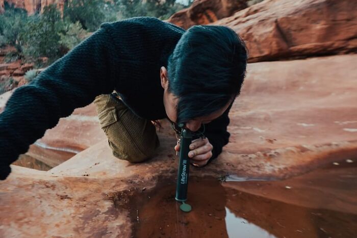 Person using a portable water filter outdoors on a rocky surface, demonstrating popular Amazon finds in nature gear.