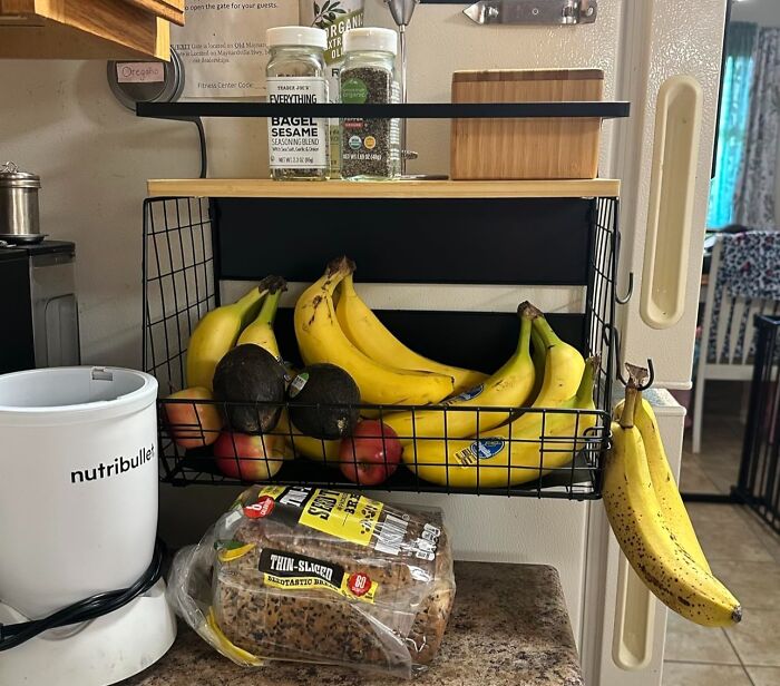 Kitchen storage with a hanging fruit basket holding bananas, avocados, and spices, a popular Amazon find for organized spaces.