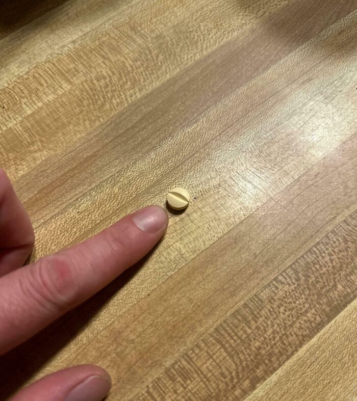 Finger pointing at a tiny pill on a wooden table, illustrating a mildly infuriated mood ruined by small annoyances.