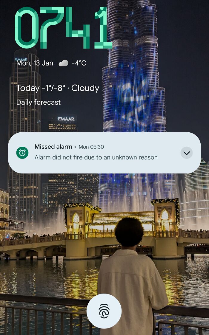 Person facing illuminated building at night with phone notification showing missed alarm, a common mood ruiner.