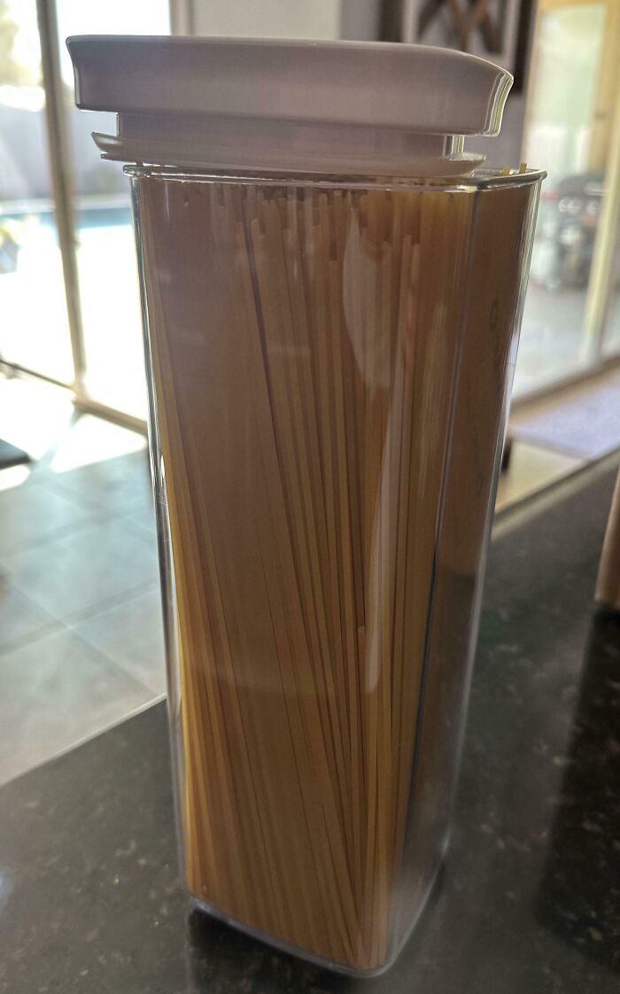 Clear container filled with uncooked spaghetti, lid not fully closed, a mildly infuriated mood ruiner in the kitchen.