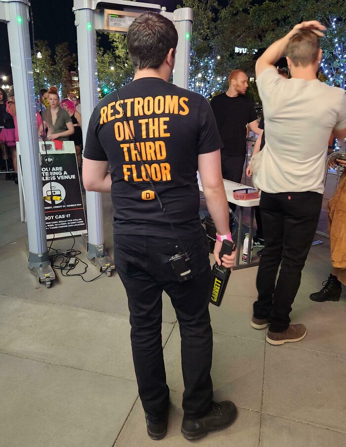 Man wearing a clever solution shirt directing people to restrooms on the third floor at a crowded event entrance.