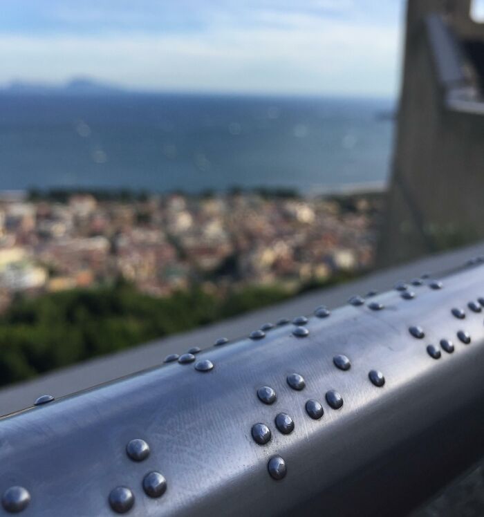 Close-up of a metal railing with Braille dots, showcasing a clever way people solved overlooked accessibility issues.