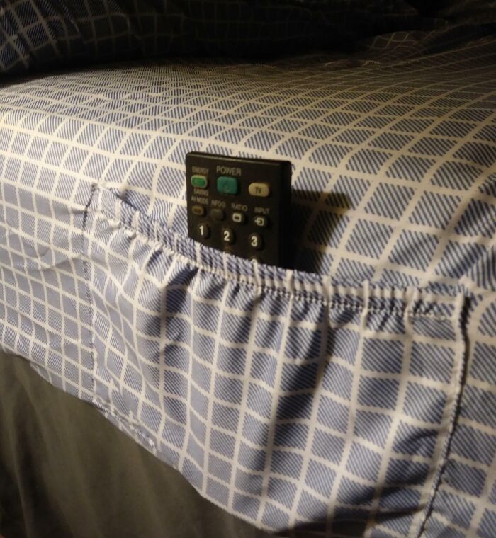 Small remote control stored in a fabric pocket attached to bed sheet, a clever way to solve overlooked storage issues.
