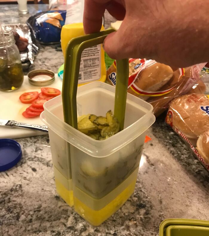Hand using a clever pickle container with built-in tongs to easily lift pickles, a smart solution for kitchen convenience.