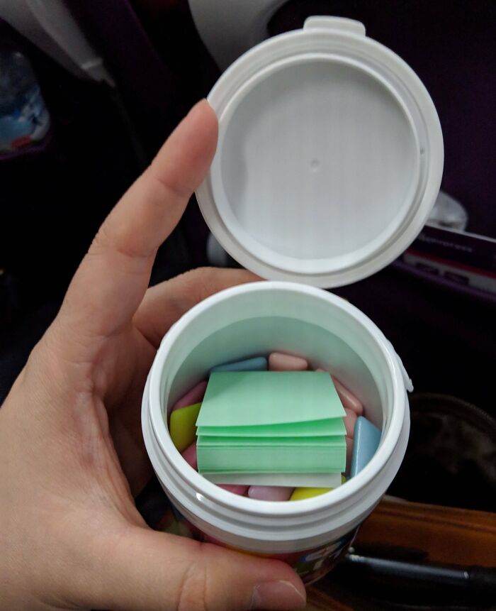 Hand holding an open container filled with colorful pills and cleverly folded paper as an overlooked solution.