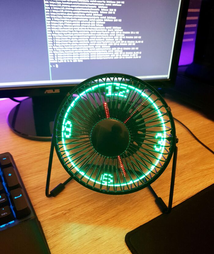 Desk setup with a small fan displaying a digital clock, showcasing clever ways people solved overlooked issues.