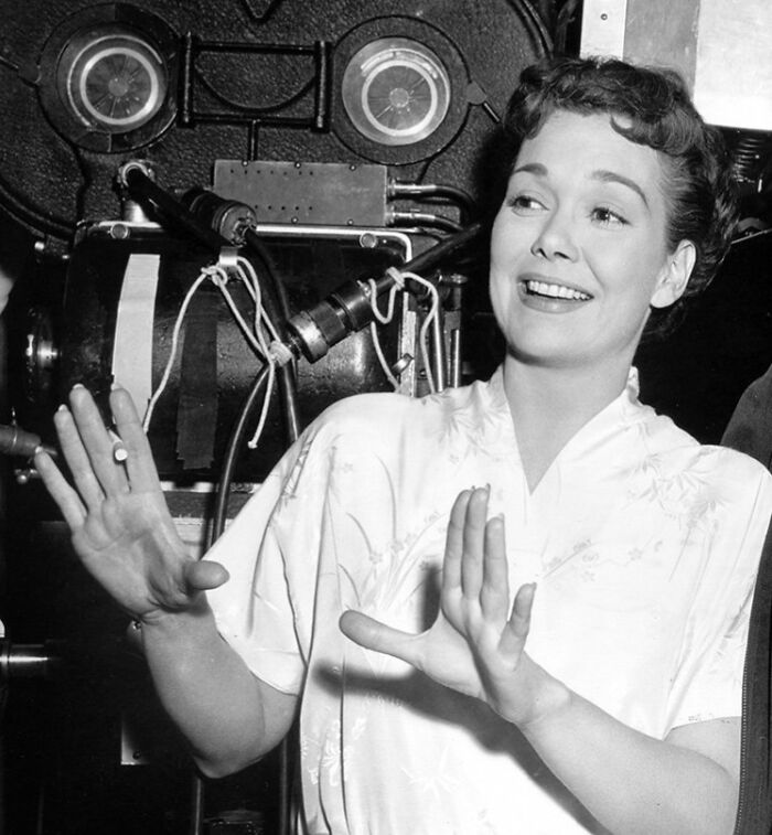Black and white photo of a glamorous 1940s Hollywood icon smiling on a movie set during filming.