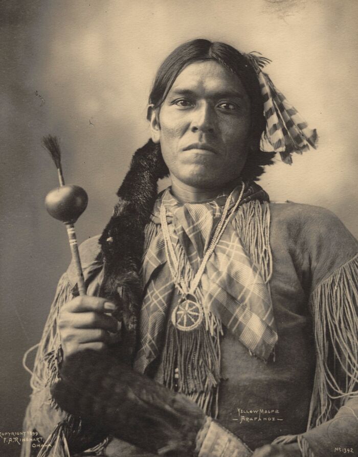 Portrait of a Native American man wearing traditional attire, holding a ceremonial object in a powerful historic portrait.