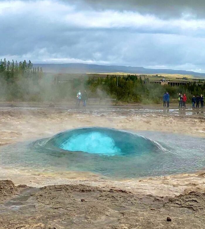 Geyser about to erupt with vibrant blue water and steam rising, capturing rare natural phenomena in a scenic landscape.